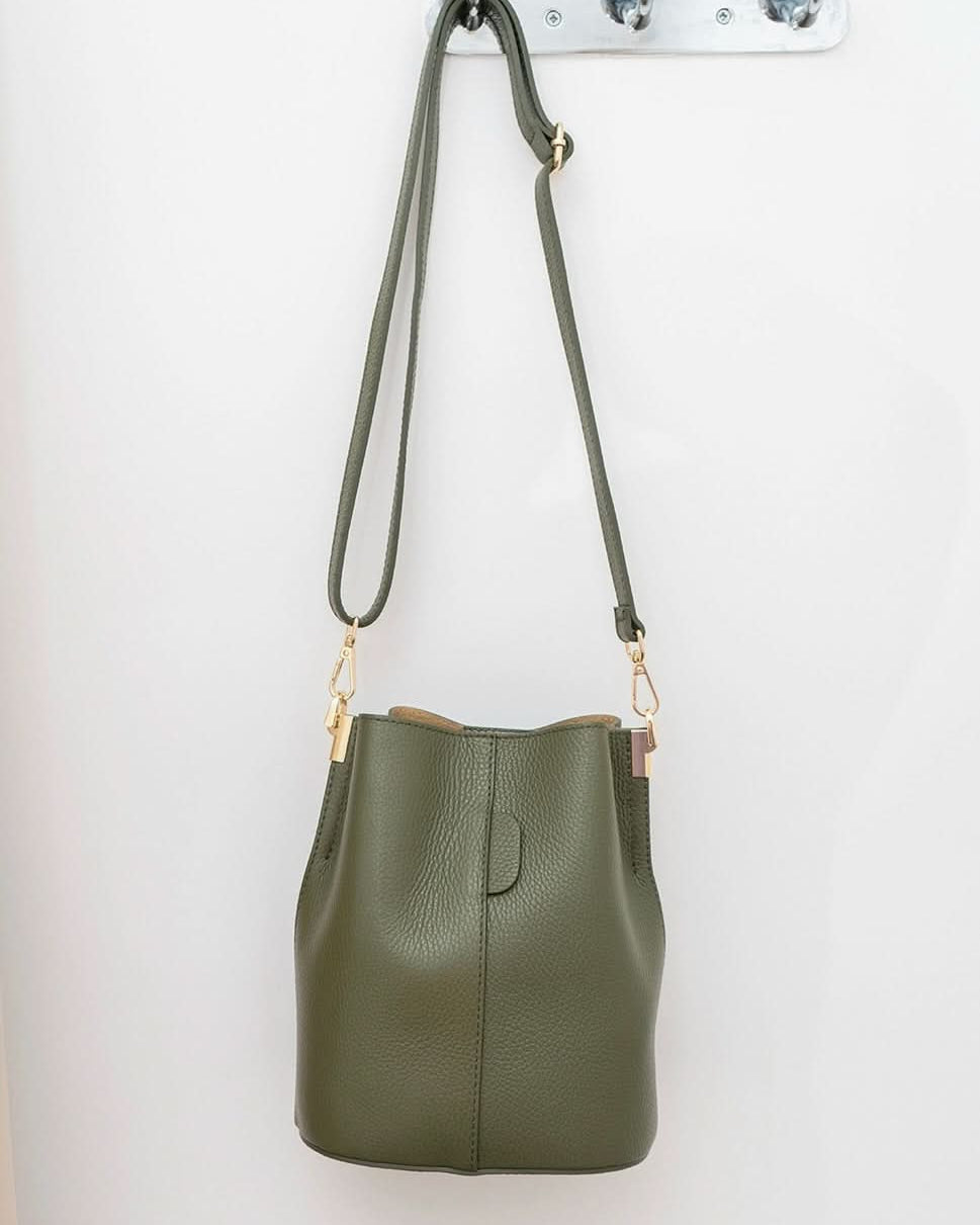 Green leather handbag with a strap hanging on a white wall.