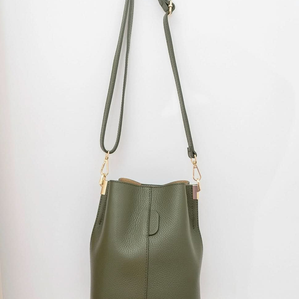 Green leather handbag with a strap hanging on a white wall.