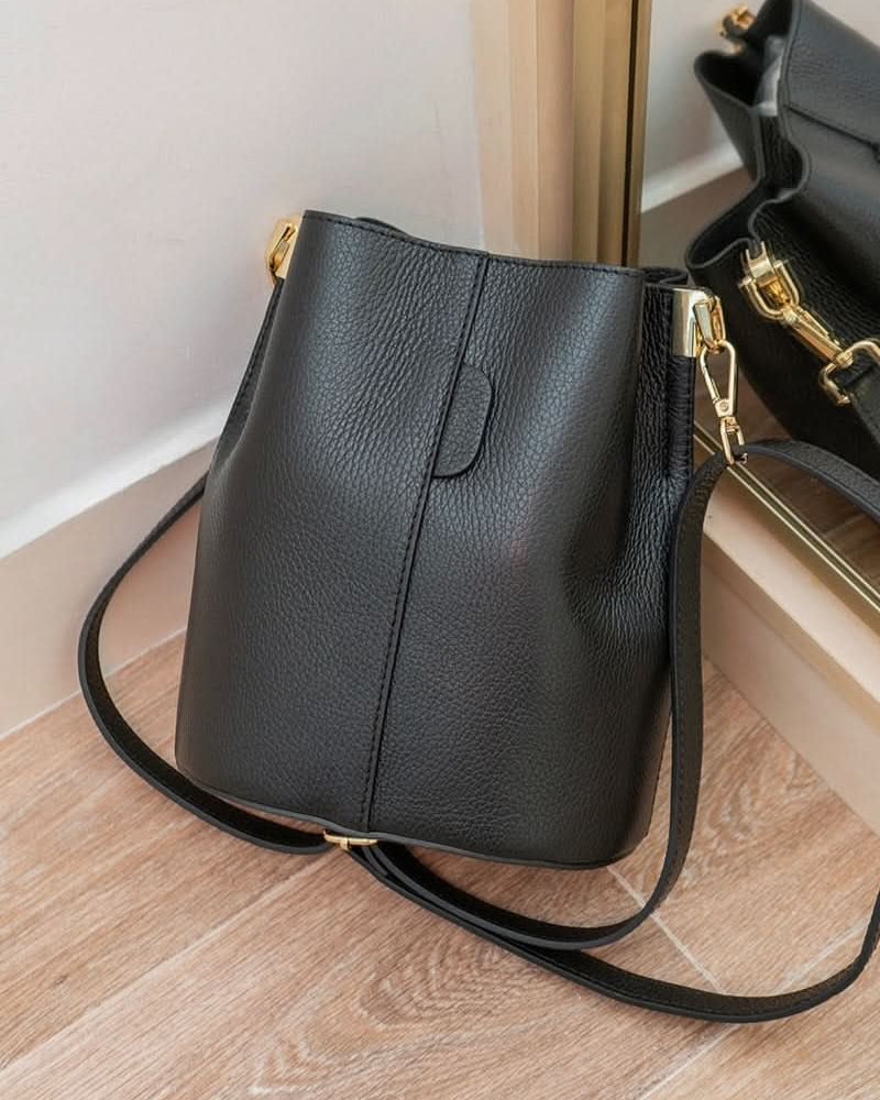 Black leather handbag with gold accents on a wooden floor
