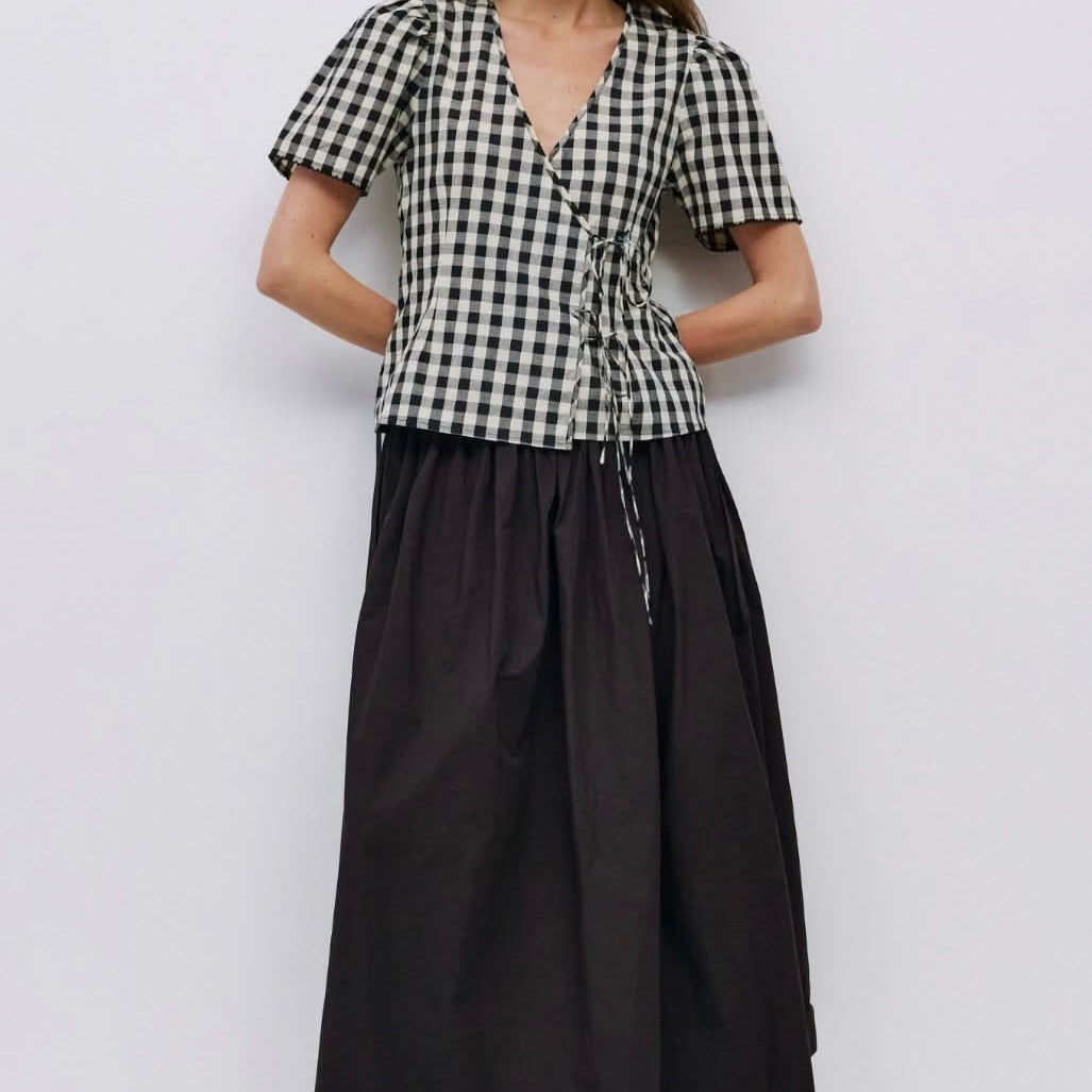 Woman wearing checkered puff sleeve blouse with 2 wrap ties in the front with black long skirt
