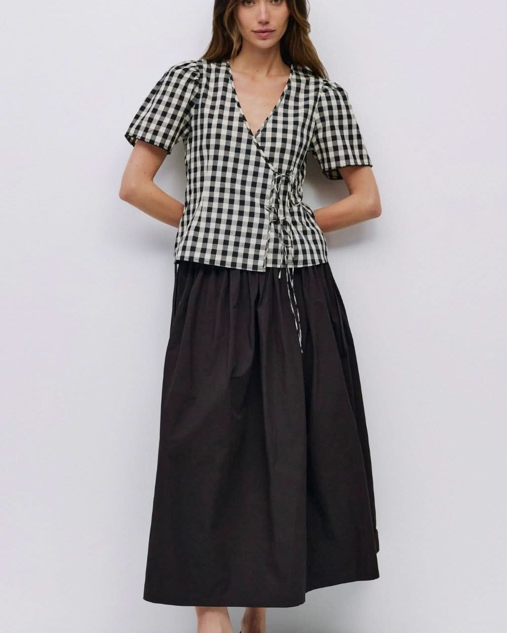 Woman wearing checkered puff sleeve blouse with 2 wrap ties in the front with black long skirt