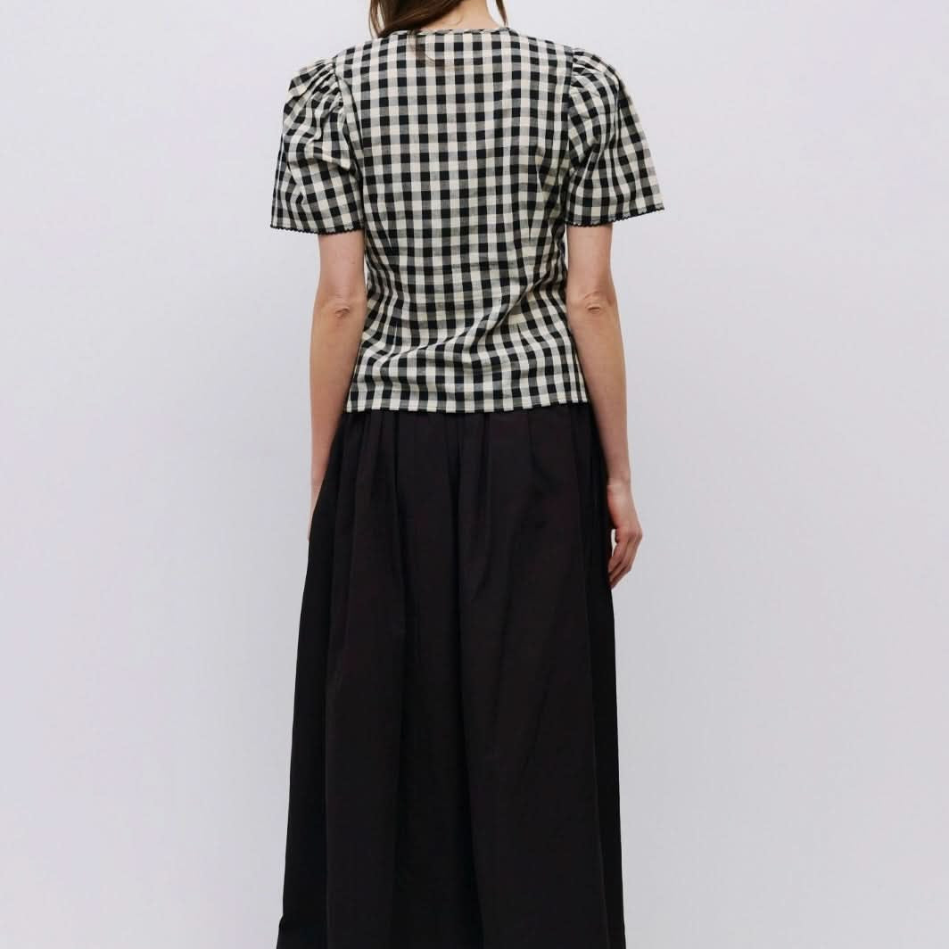 Woman facing backward wearing checkered puff sleeve blouse with black long skirt