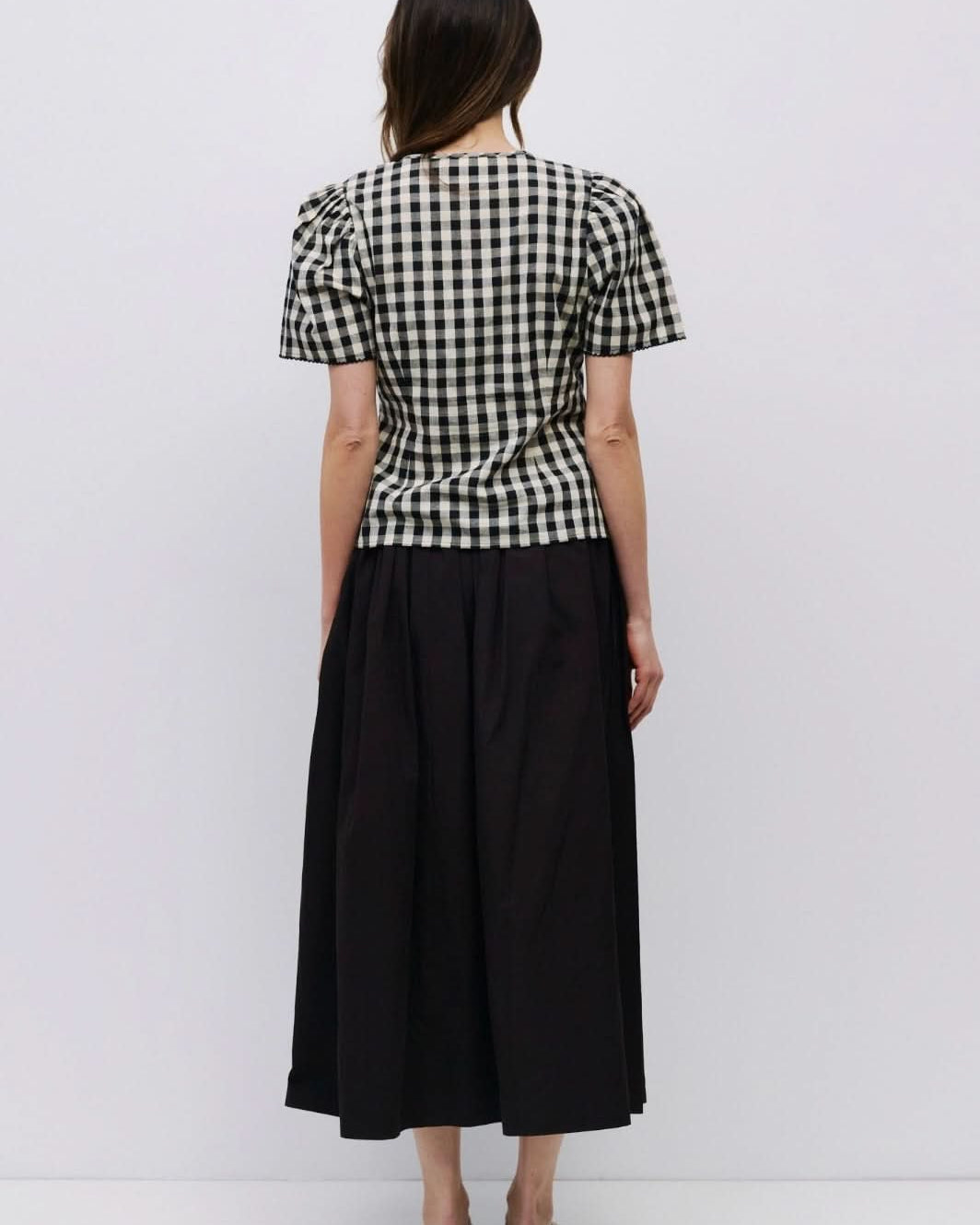 Woman facing backward wearing checkered puff sleeve blouse with black long skirt