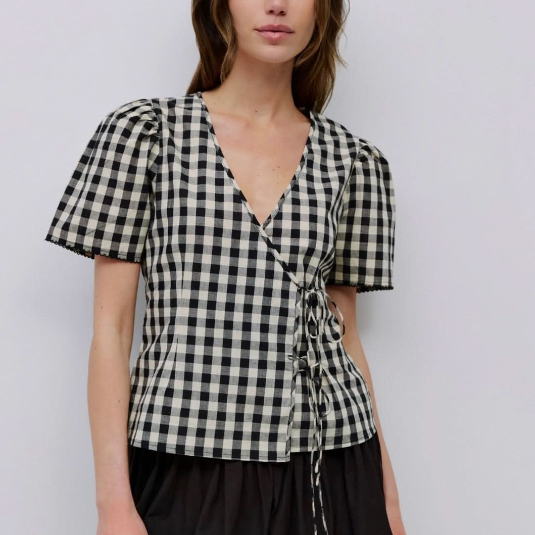 Woman wearing checkered puff sleeve blouse with 2 wrap ties in the front with black long skirt
