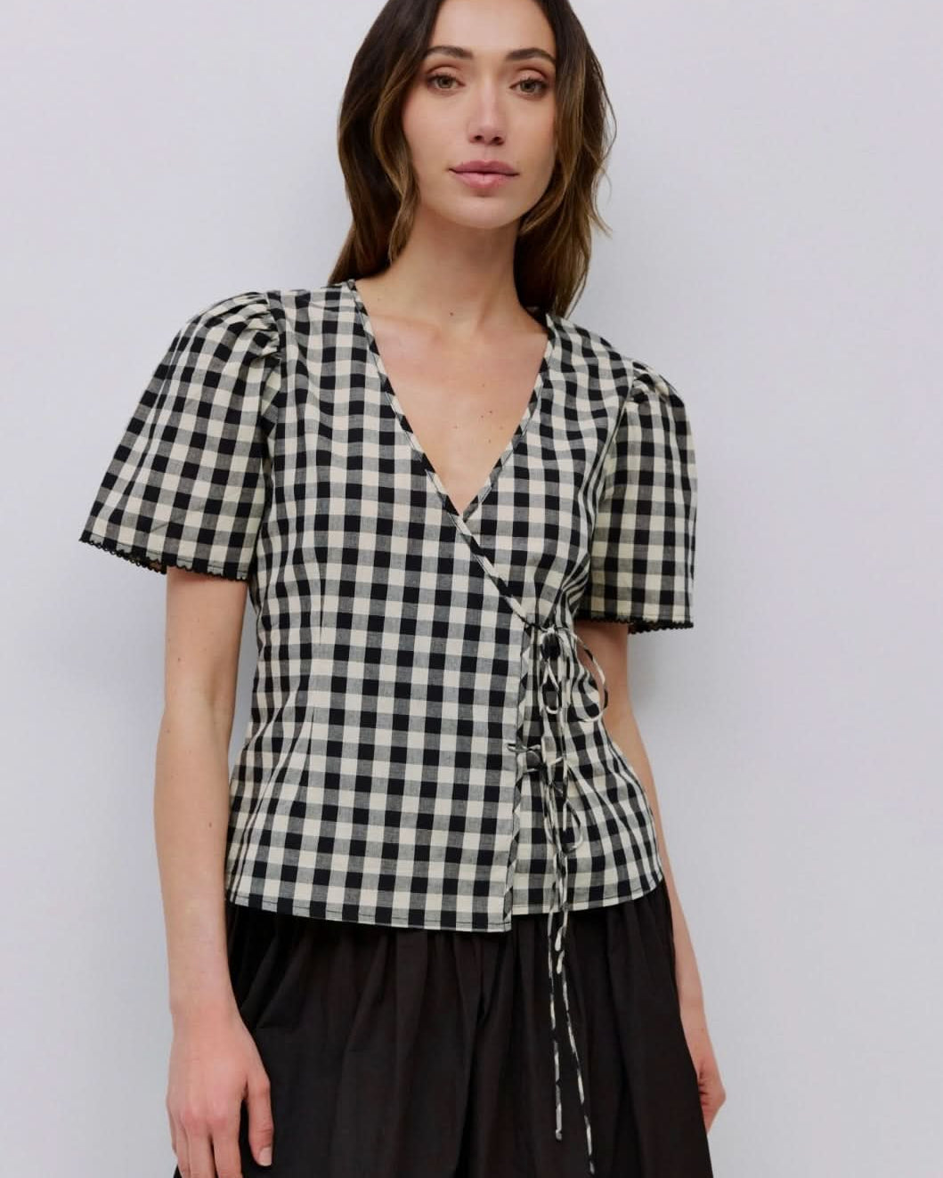 Woman wearing checkered puff sleeve blouse with 2 wrap ties in the front with black long skirt