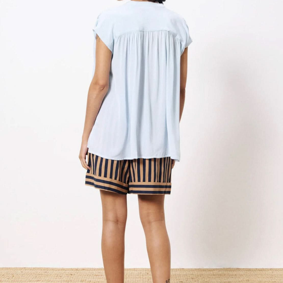 Woman turned backward wearing lightweight light blue blouse paired with tan and black dress shorts