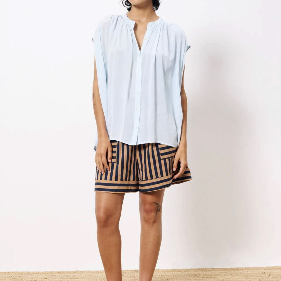 Woman wearing lightweight light blue blouse button closure paired with tan and black dress shorts