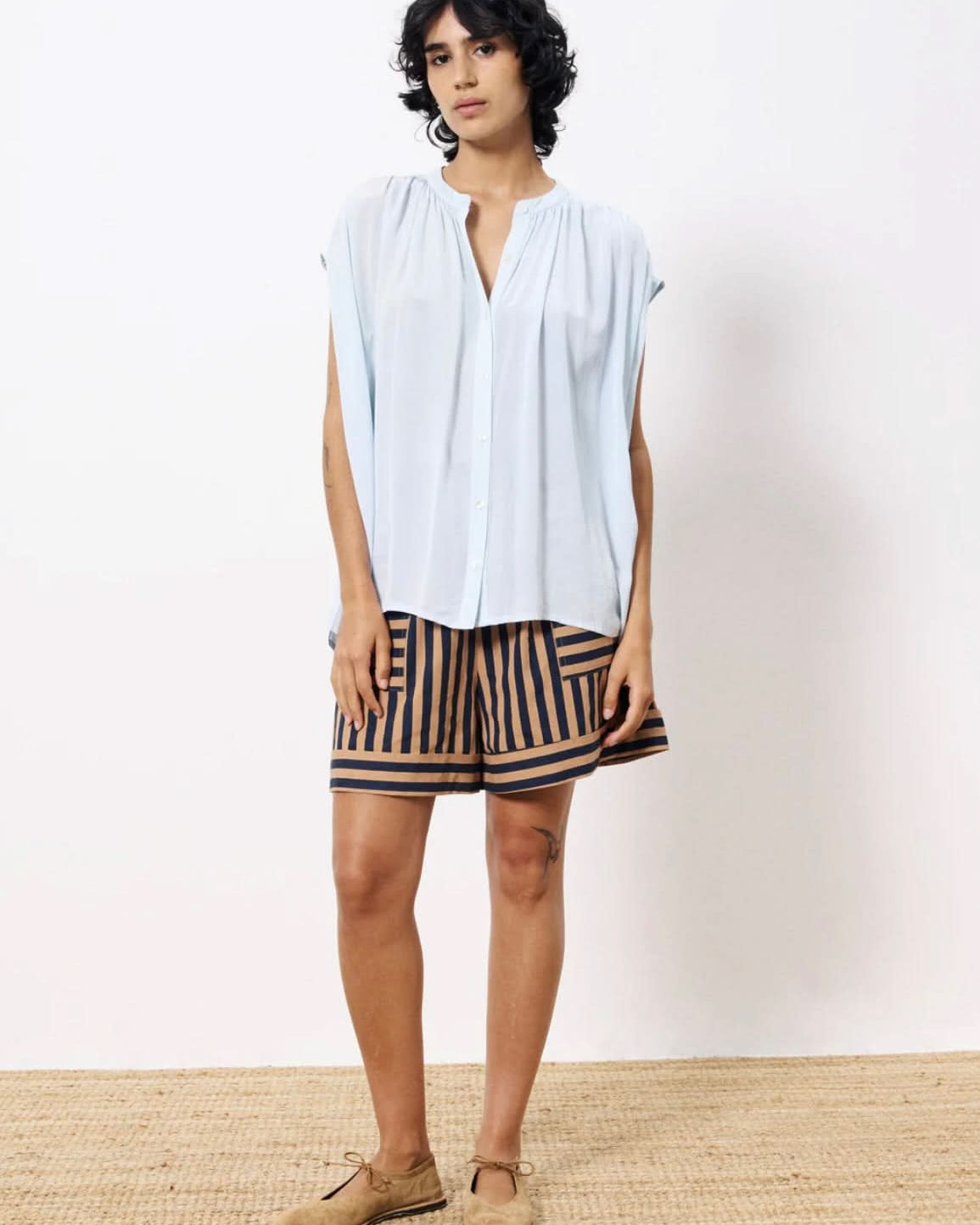 Woman  wearing lightweight light blue blouse button closure paired with tan and black dress shorts