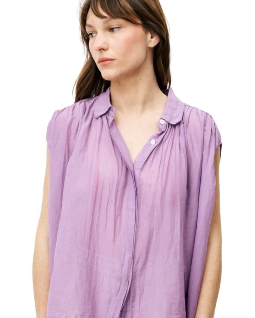 Woman wearing purple silky cotton button up, purple blouse, standing against white wall