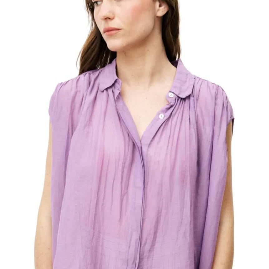 Woman wearing purple silky cotton button up, purple blouse, standing against white wall
