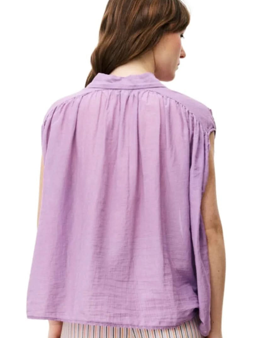 Woman wearing purple silky cotton button up, purple blouse, standing against white wall