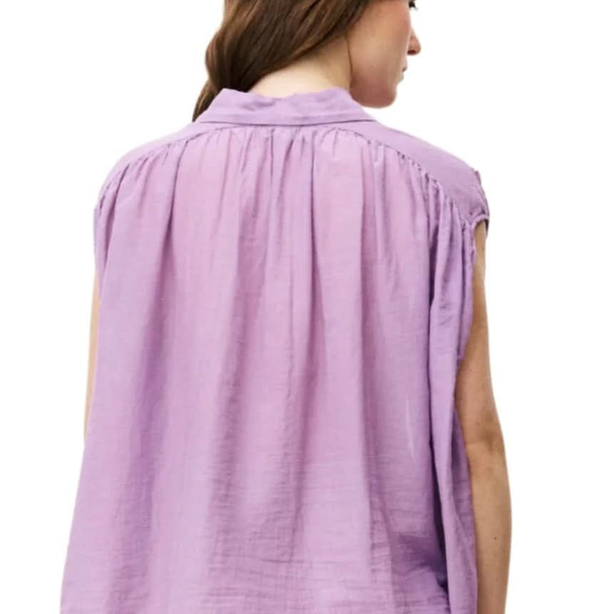 Woman wearing purple silky cotton button up, purple blouse, standing against white wall