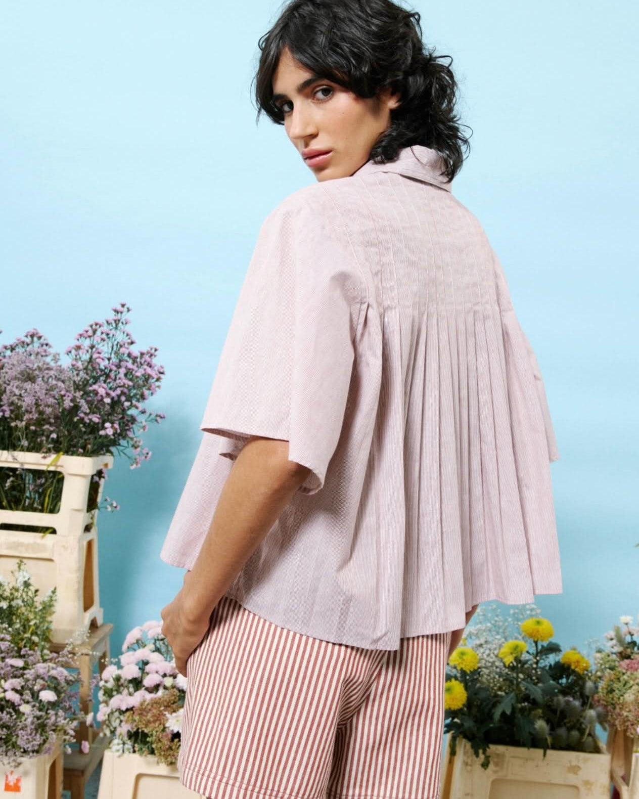 Woman wearing 100% cotton button down, cropped blouse with small vertical stripes and pleated detail in the back