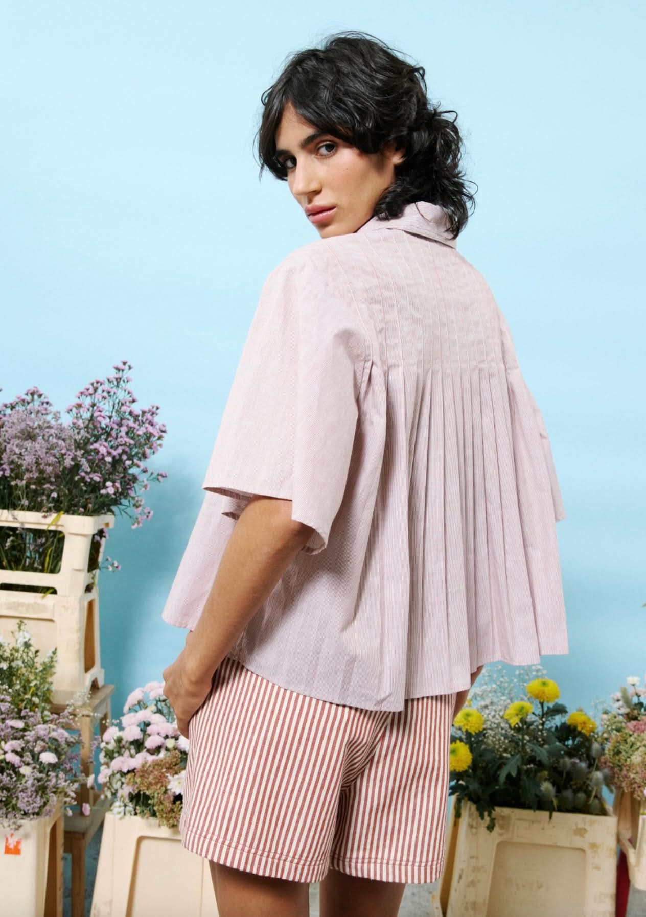 Woman wearing 100% cotton button down, cropped blouse with small vertical stripes and pleated detail in the back
