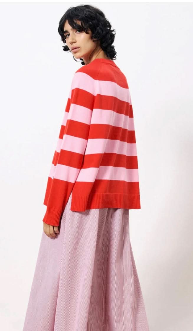 Woman wearing pink and red horizontal thick striped sweater standing against a blank wall
