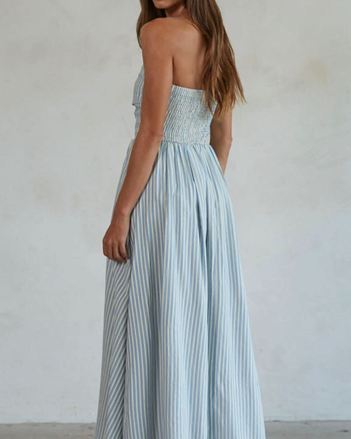 Woman wearing white and green/blue vertically striped, sleeveless maxi dress standing against a blank wall