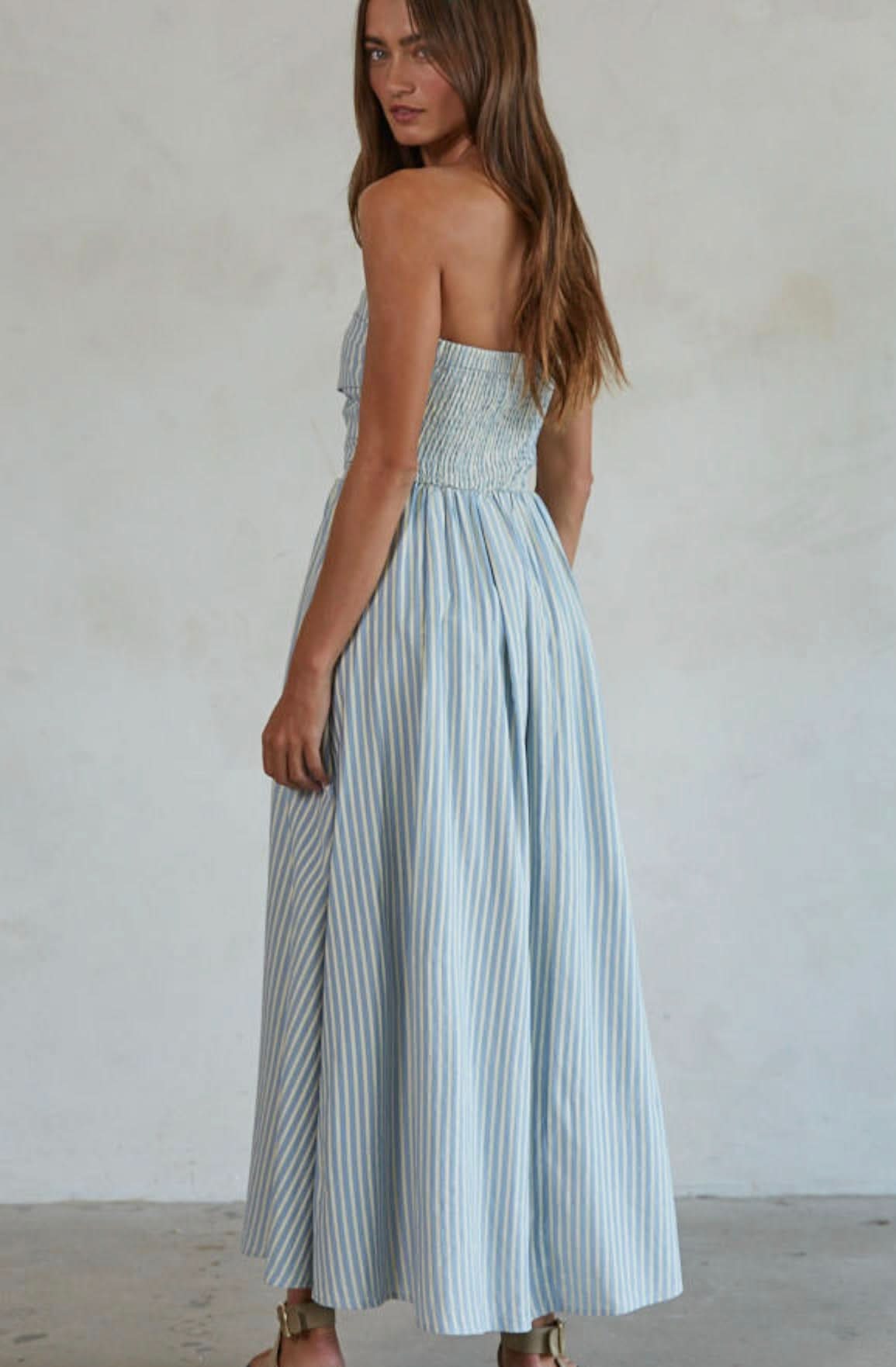 Woman wearing white and green/blue vertically striped, sleeveless maxi dress standing against a blank wall
