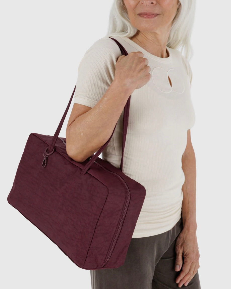 Woman holding a maroon BAGGU bag against a white background