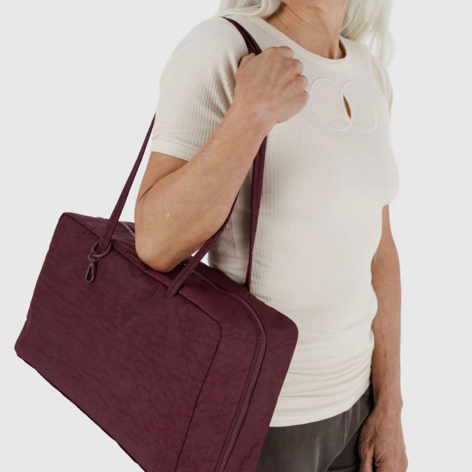 Woman holding a maroon BAGGU bag against a white background