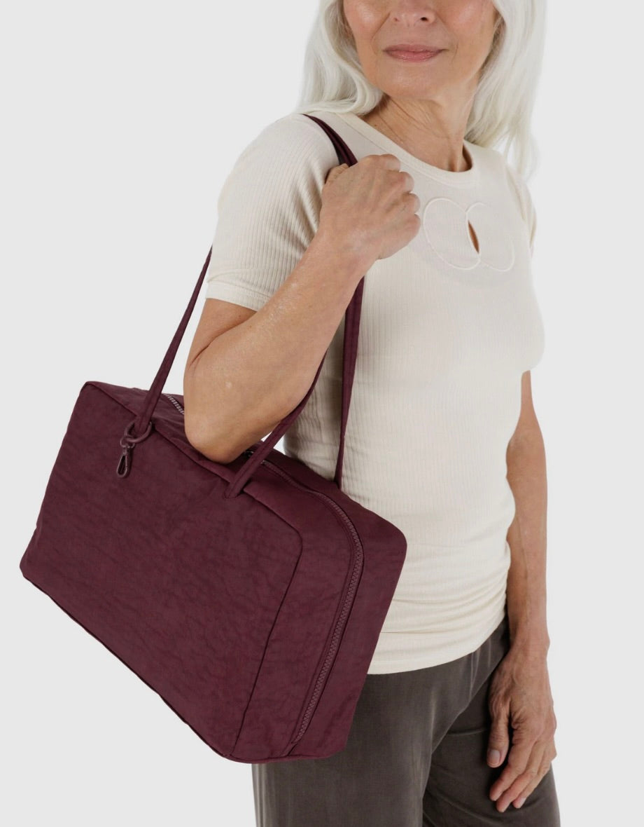 Woman holding a maroon BAGGU bag against a white background