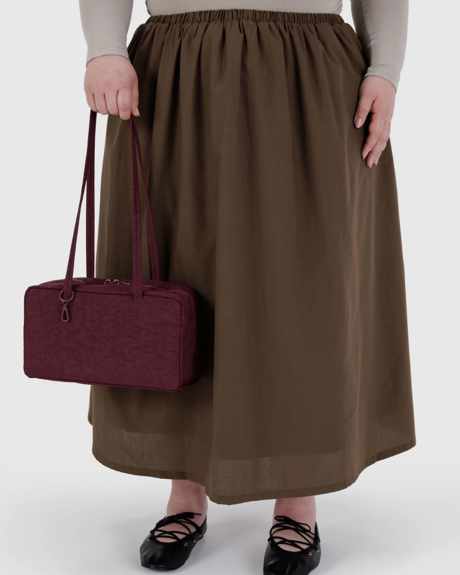 Person wearing a brown skirt holding a maroon handbag on a white background
