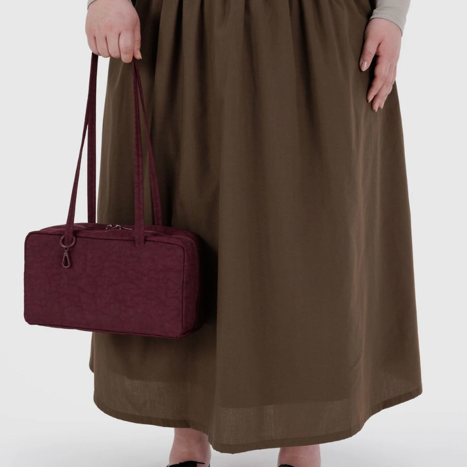 Person wearing a brown skirt holding a maroon handbag on a white background