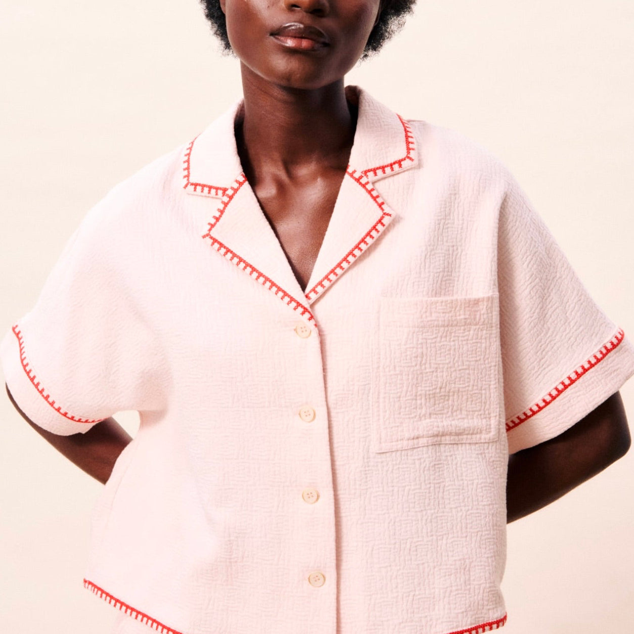 Woman wearing a white outfit with red trim on a plain background
