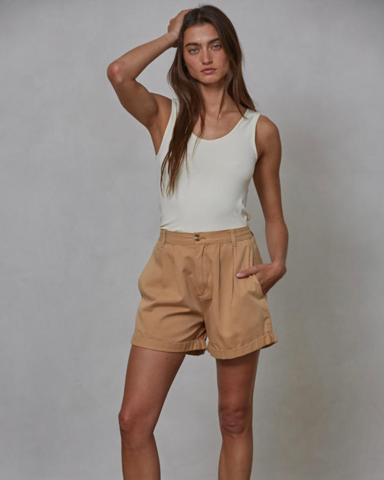 Woman wearing a white tank top and beige shorts against a plain background