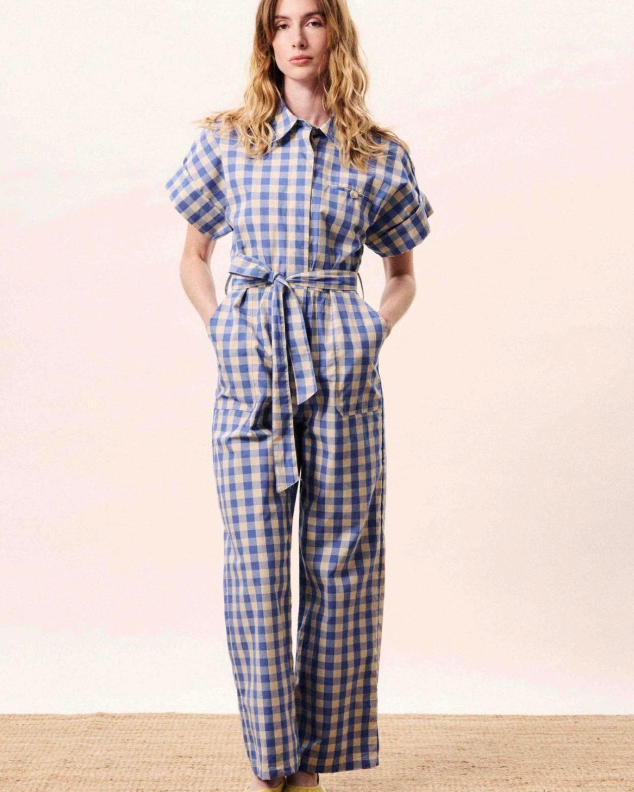 Woman wearing a blue and white checkered jumpsuit on a light pink background
