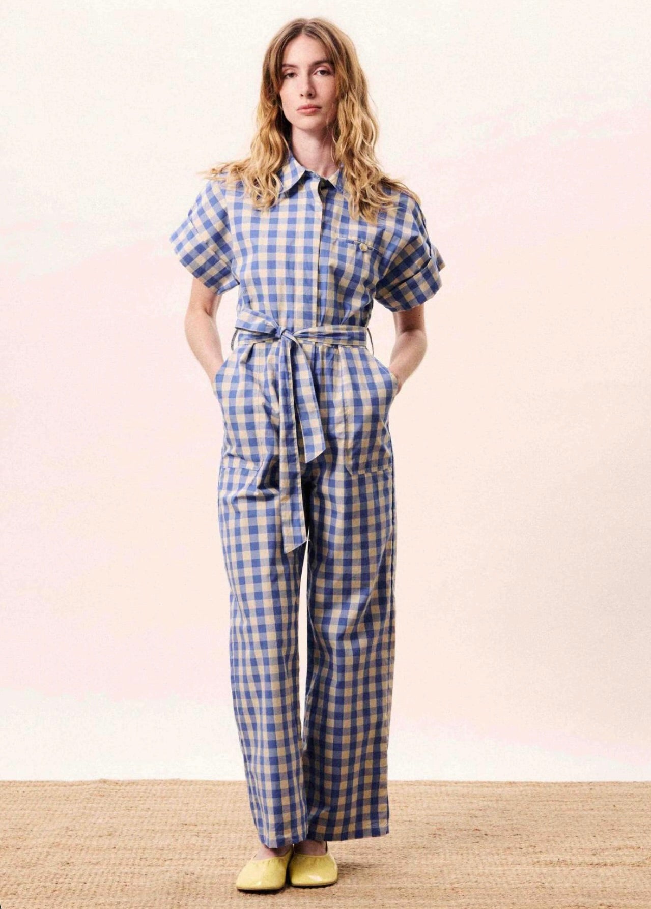 Woman wearing a blue and white checkered jumpsuit on a light pink background