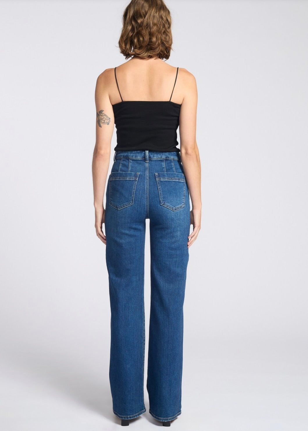 Person wearing blue jeans and a black top on a white background