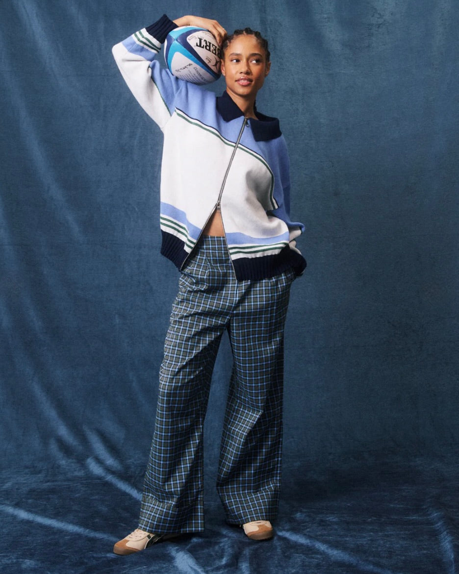 Person wearing a blue and white outfit with plaid pants, holding a sports ball against a blue backdrop.