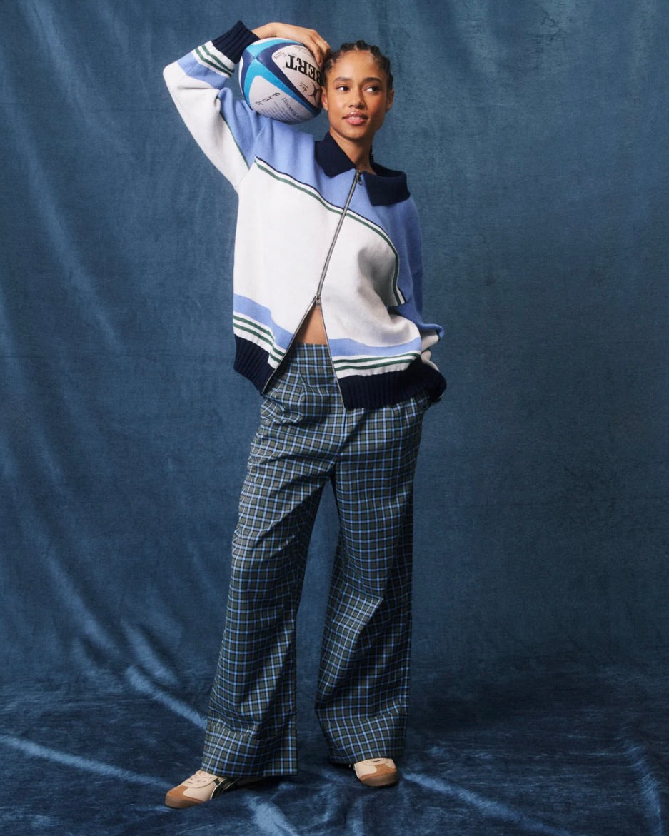 Person wearing a blue and white outfit with plaid pants, holding a sports ball against a blue backdrop.