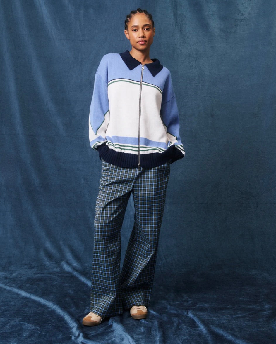 Person wearing a blue and white sweater with plaid pants on a blue background