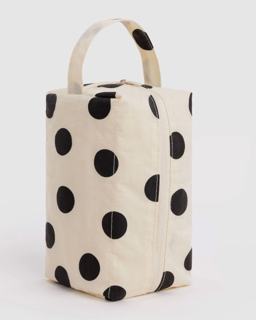 A cream-colored canvas lunch bag with a black polka dot pattern and a top handle, shown on a light gray background.