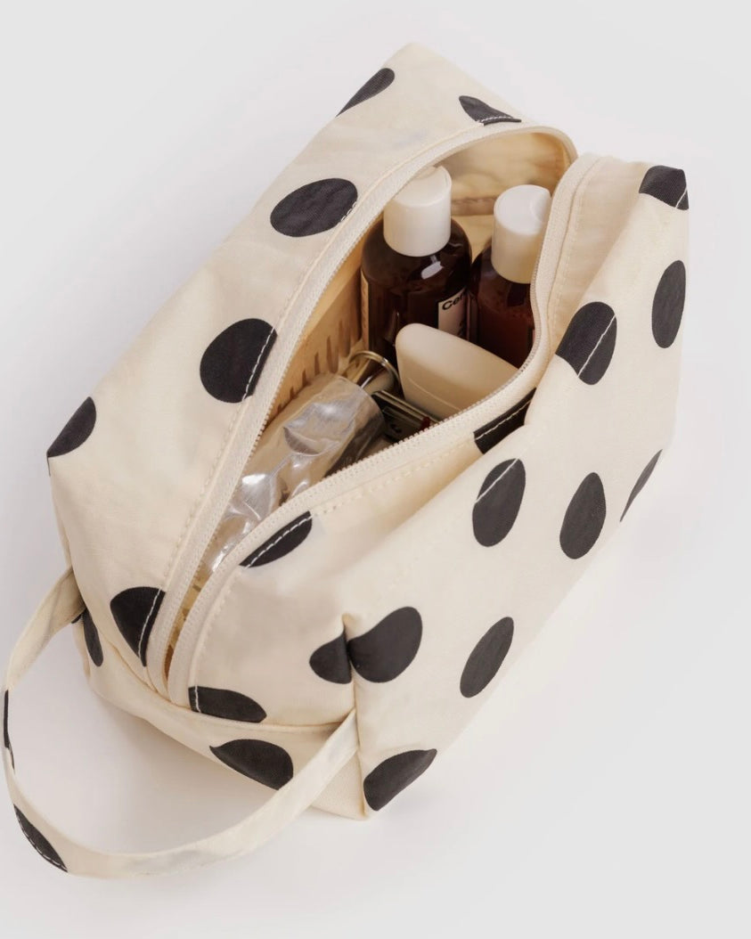 An off-white canvas cosmetic bag with large black polka dots, shown open with toiletry bottles inside, on a plain white background.