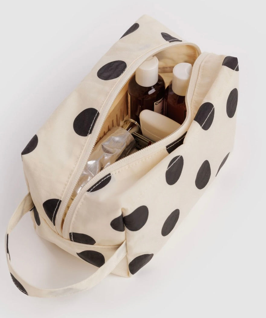 An off-white canvas cosmetic bag with large black polka dots, shown open with toiletry bottles inside, on a plain white background.