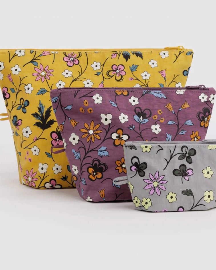 Three fabric zip pouches with floral prints in yellow, mauve, and light gray, arranged by size on a white background.