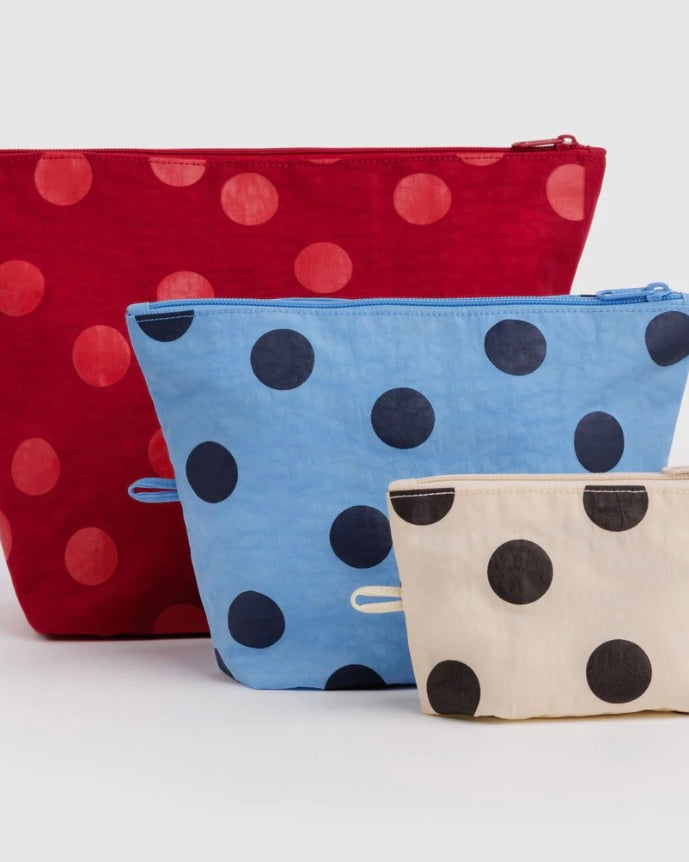 Three fabric zip pouches with a polka dot pattern, displayed in a size gradient. The largest pouch is red with pinkish-red dots, the middle pouch is light blue with dark blue dots, and the smallest pouch is cream with dark brown dots.