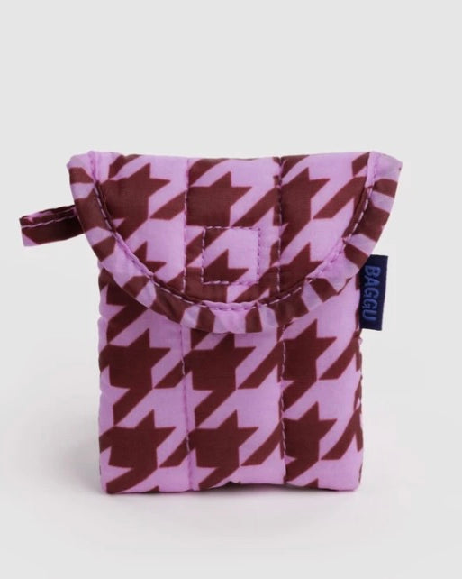 A small quilted pouch with a purple and brown houndstooth pattern, featuring a top handle and a small navy blue tag with the brand name BAGGU.