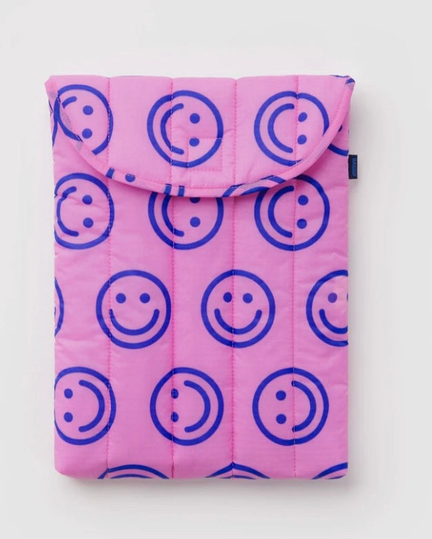 A pink quilted tablet sleeve featuring a repeating blue smiley face pattern, shown flat against a light gray background.