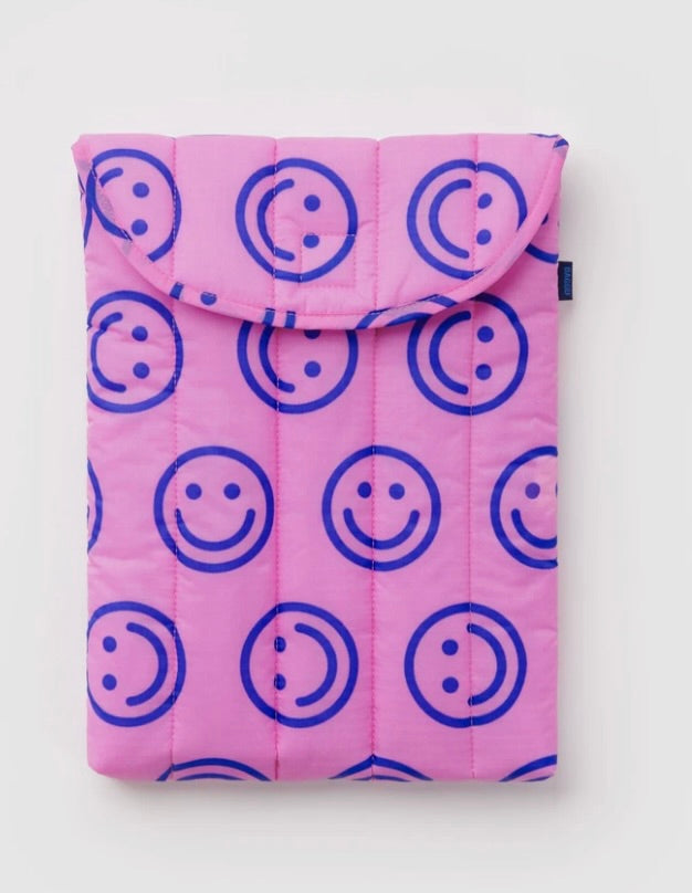 A pink quilted tablet sleeve featuring a repeating blue smiley face pattern, shown flat against a light gray background.