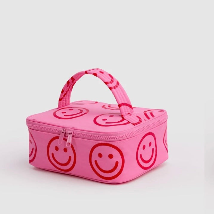 A pink zippered lunch bag with a top handle, featuring an all-over red smiley face pattern, photographed on a light gray background.
