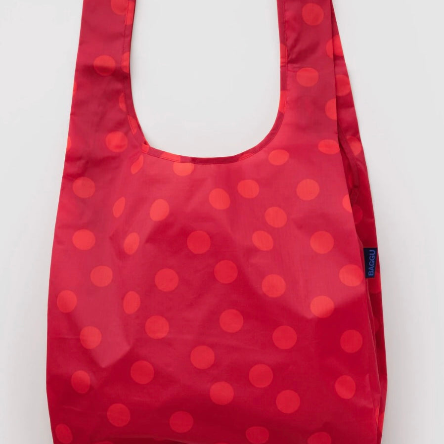 A reusable folding shopping bag in red with a pattern of darker red polka dots, shown against a plain light gray background.