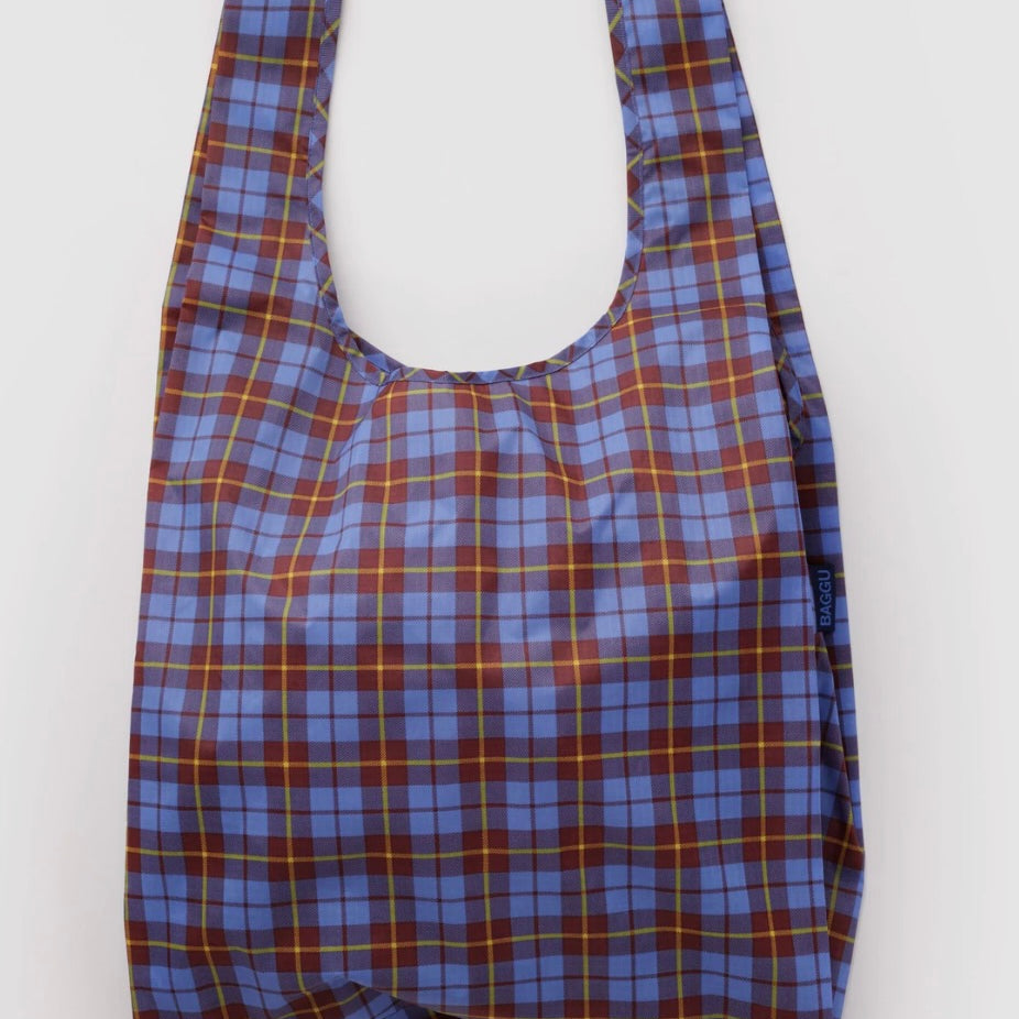 A reusable plastic shopping bag with a blue, brown, and yellow plaid pattern, shown against a plain light gray background.