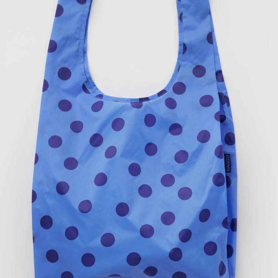 A reusable plastic shopping bag with a blue and dark purple polka dot pattern, shown against a plain light gray background.