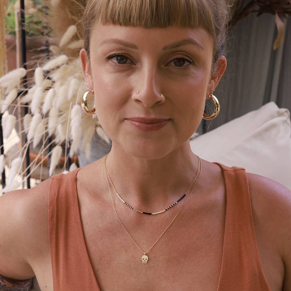 Woman wearing gold hoop earrings and a necklace with a pendant, standing outdoors.