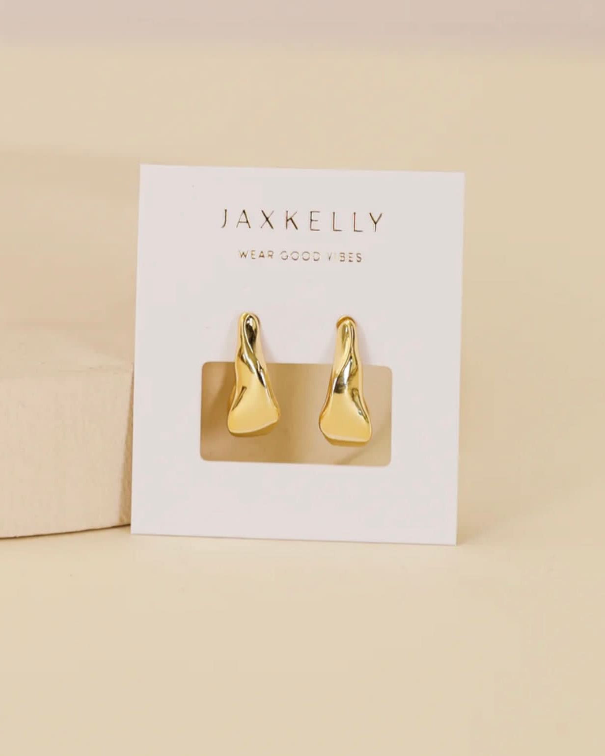 Gold earrings on a Jaxkelly branded card against