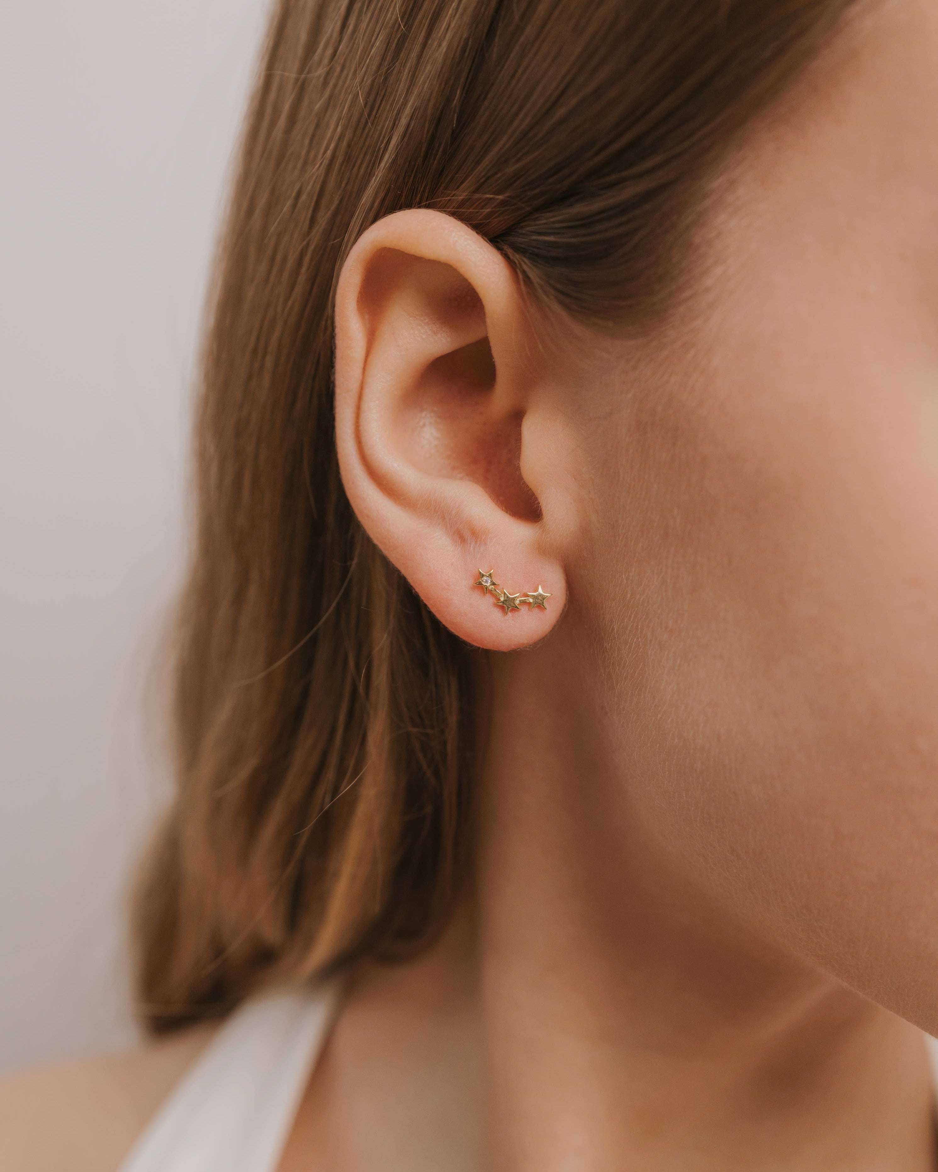 Close-up of an ear wearing a small gold earring stars earings