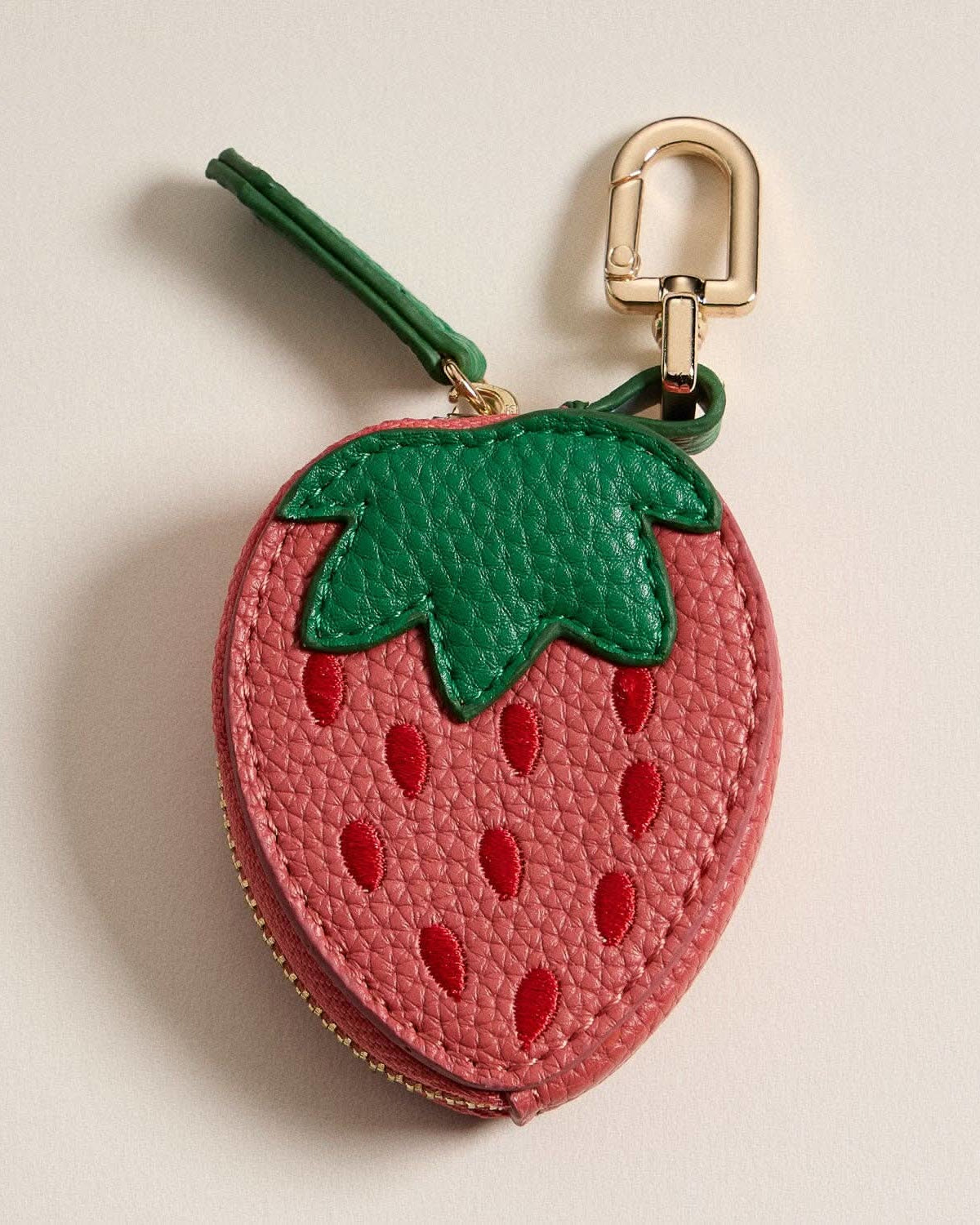 Strawberry-shaped keychain with a gold clasp on a beige background
